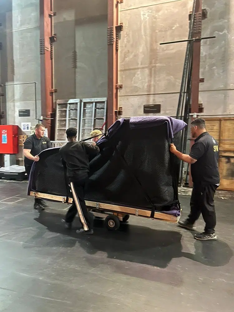 Specialist Piano Movers crew moving a wrapped grand piano on a piano board and dolly